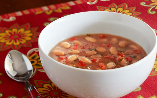 white bowl with pink beans on a brightly colored table cloth with a spoon on the side